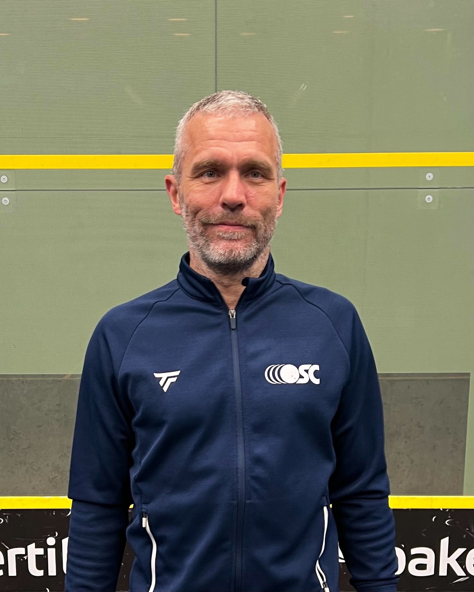 Billede af kasserer i OSC, Brian Blomholt, i sportstøj foran en squashbane.
