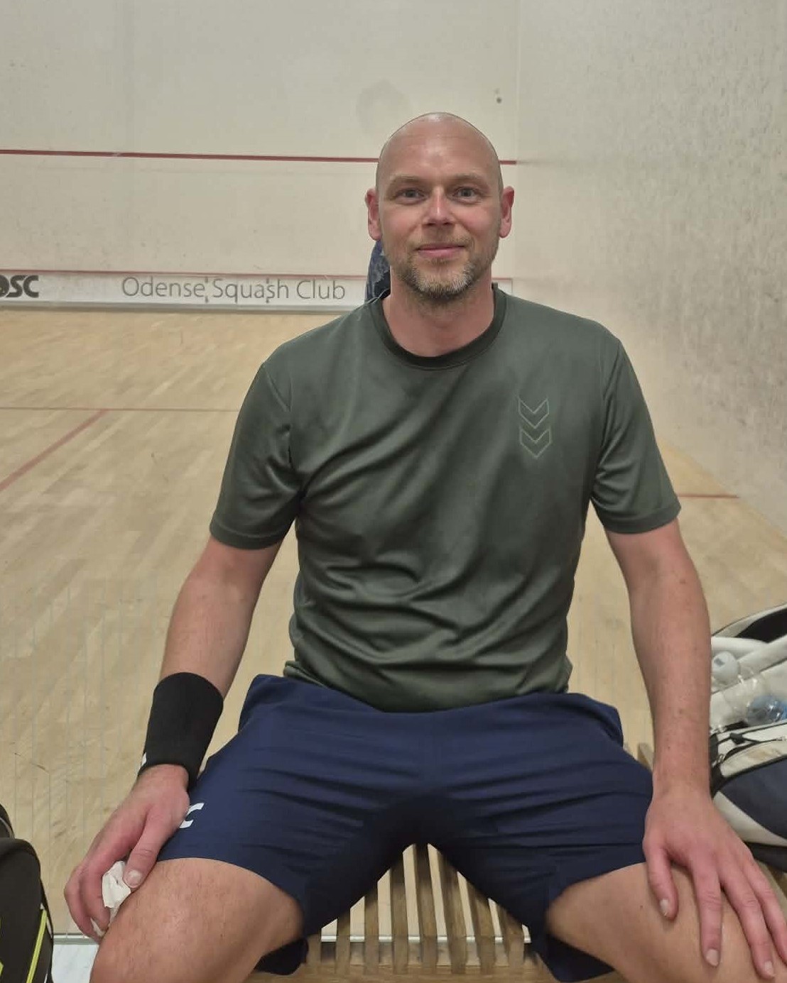 Billede af næstformand for OSC, Dennis Hansen, i sportstøj foran en squashbane.