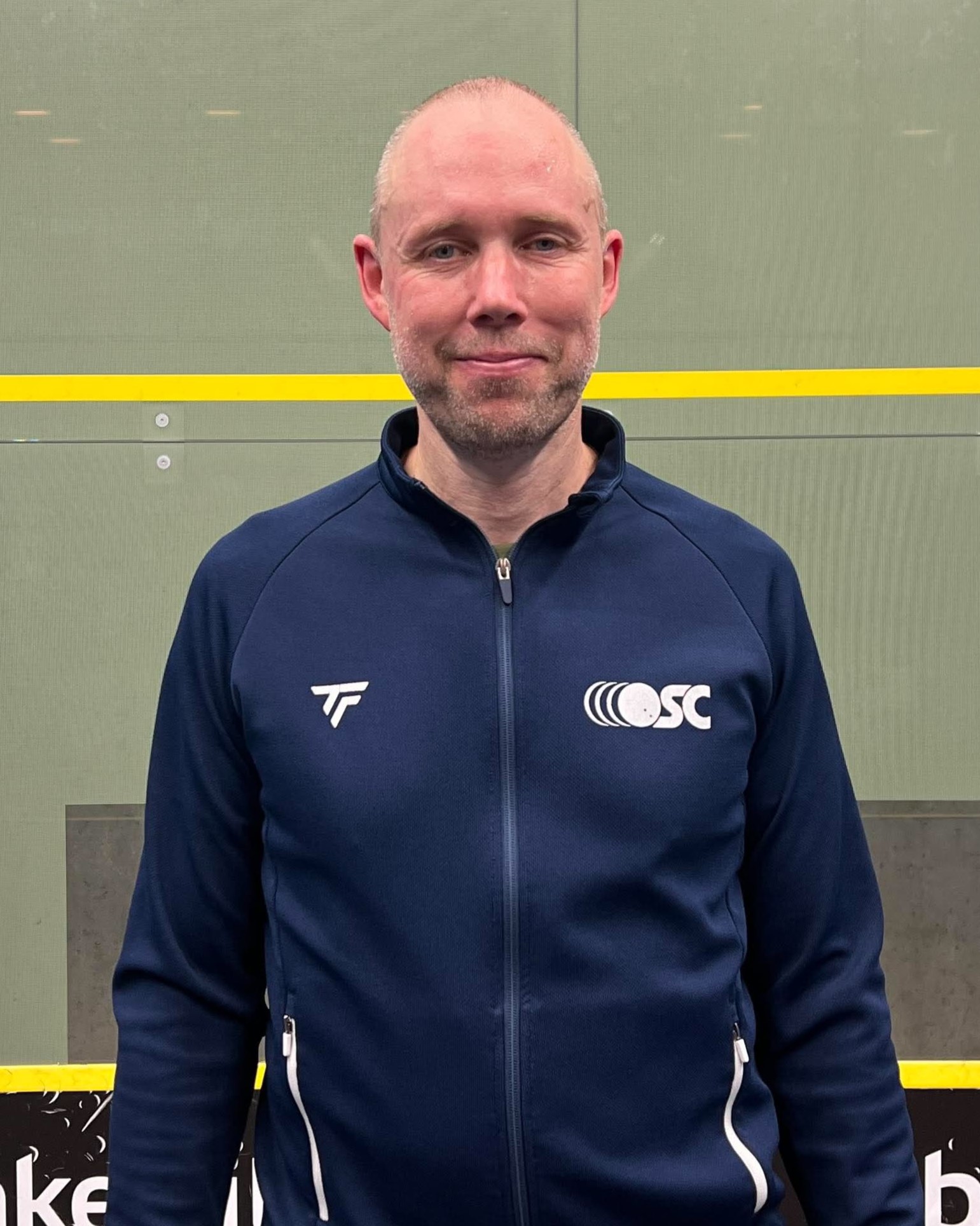 Billede af bestyrelsesmedlem i OSC, Kim Pedersen, i sportstøj foran en squashbane.